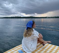 a woman sitting on top of a yellow and white checkered table cloth next to the ocean