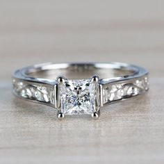 a princess cut diamond engagement ring with filigrees on the sides, set in 18k white gold