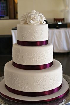 a three tiered white wedding cake with purple ribbon