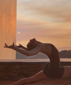 a woman is doing yoga outside in front of a wall and water fountain at sunset