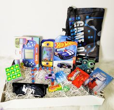 a box filled with assorted toys and games on top of a white blanket next to a black bag