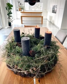 a wooden table topped with candles surrounded by greenery and pineconuts on top of it