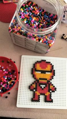 a plastic container filled with lots of colorful beads next to a lego iron man figure