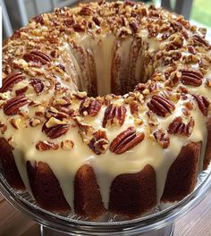 a bundt cake with pecans and icing sitting on a glass platter