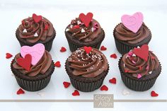 chocolate cupcakes decorated with hearts and sprinkles on a white surface