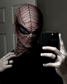 a person taking a selfie with their phone in front of him wearing a spiderman mask