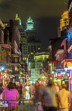 many people are walking down the street at night in an urban area with tall buildings and neon lights