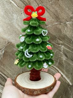 a hand holding a small christmas tree on top of a piece of wood