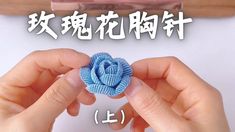 two hands holding a blue cloth flower in front of a piece of paper with chinese writing on it