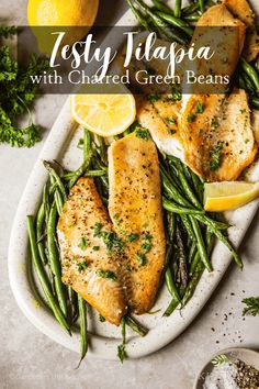 fish and green beans on a plate with lemon wedges