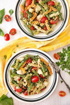 two plates filled with pasta salad on top of a yellow towel next to a fork