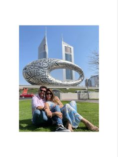 two people sitting on the grass in front of a building with graffiti written on it