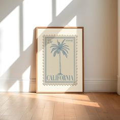 a framed stamp with a palm tree is on the floor in front of a white wall