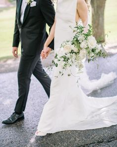 a bride and groom holding hands walking down the street in front of a large tree