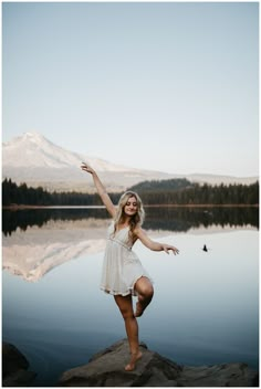 a woman standing on top of a rock next to a lake