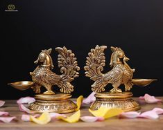 two golden rooster figurines sitting next to each other on top of a wooden table