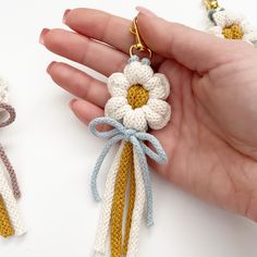 the hand is holding two crocheted key chains with flowers on each one and a chain attached to it