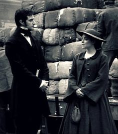 a man and woman standing next to each other in front of stacks of bags on the street