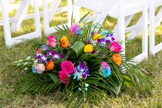 a bouquet of colorful flowers sitting on top of a grass covered field next to white chairs