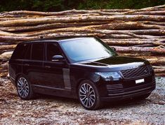 a black range rover parked in front of a pile of logs with trees behind it