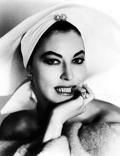 a black and white photo of a woman with her hand on her chin wearing a turban