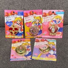 three sailor moon rings are on display in front of two other packagings, one is gold and the other is pink