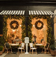 a store front with christmas wreaths on the windows and chairs in front of it