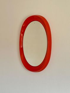 a round mirror mounted to the side of a white wall next to a red sink