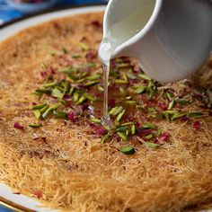 a person pouring milk on top of a cake covered in sprouts and pistachios