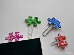 three different colored paper clips sitting on top of a white table next to a binder