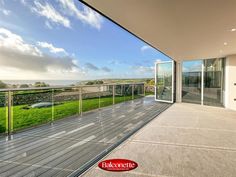 an empty balcony with sliding glass doors leading out to the ocean and grassy field behind it