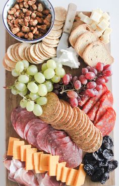 an assortment of cheeses, meats and crackers on a cutting board