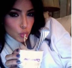 a woman is drinking out of a cup while laying on a bed with her tongue hanging out