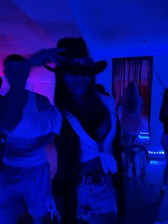 two people are dancing in a room with blue lights and one person is wearing a cowboy hat