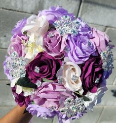 a bridal bouquet made up of purple and white flowers with crystal brooches