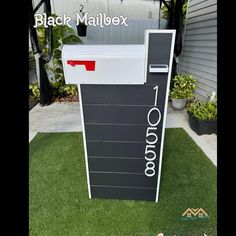 a mailbox sitting in the grass next to a house with black and white letters on it