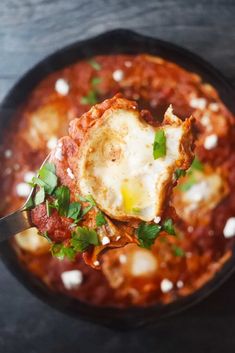 an egg is being scooped from a skillet filled with tomato sauce and parsley