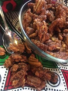 a bowl filled with nuts next to two spoons on a colorful tablecloth covered table