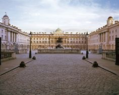 an empty courtyard with statues and buildings in the background