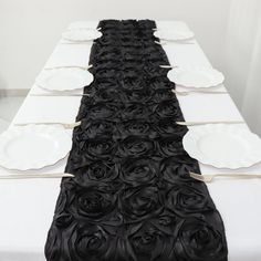 the table is set with black roses and white plates on it, ready to be served