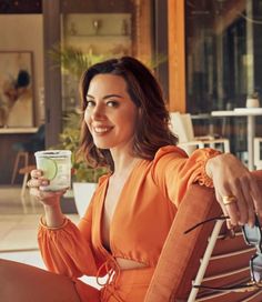 a woman in an orange dress sitting on a brown chair holding a cup and smiling