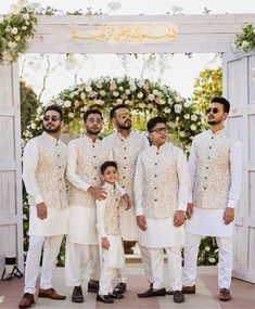 a group of men standing next to each other in front of a white arch with flowers