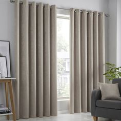 a living room with a couch, chair and window covered in beige linens that are open