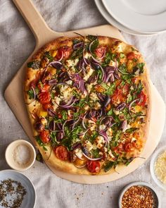 a pizza sitting on top of a wooden cutting board next to bowls and sauces