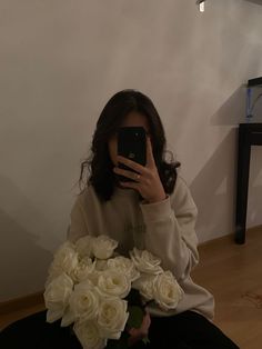 a woman sitting on the floor taking a selfie with flowers in front of her