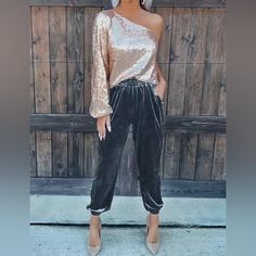 a woman standing in front of a wooden wall wearing black velvet pants and an off the shoulder top