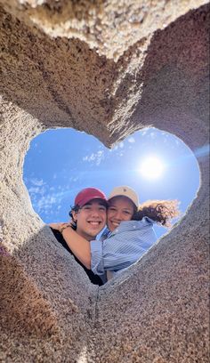 two people in a heart shaped hole with the sun shining behind them and blue sky