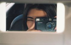 a woman holding up a camera in front of her face and looking through the window