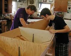 two men working on a wooden boat in a shop