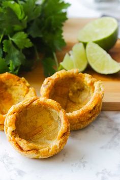 three mini pies on a cutting board with limes and cilantro in the background